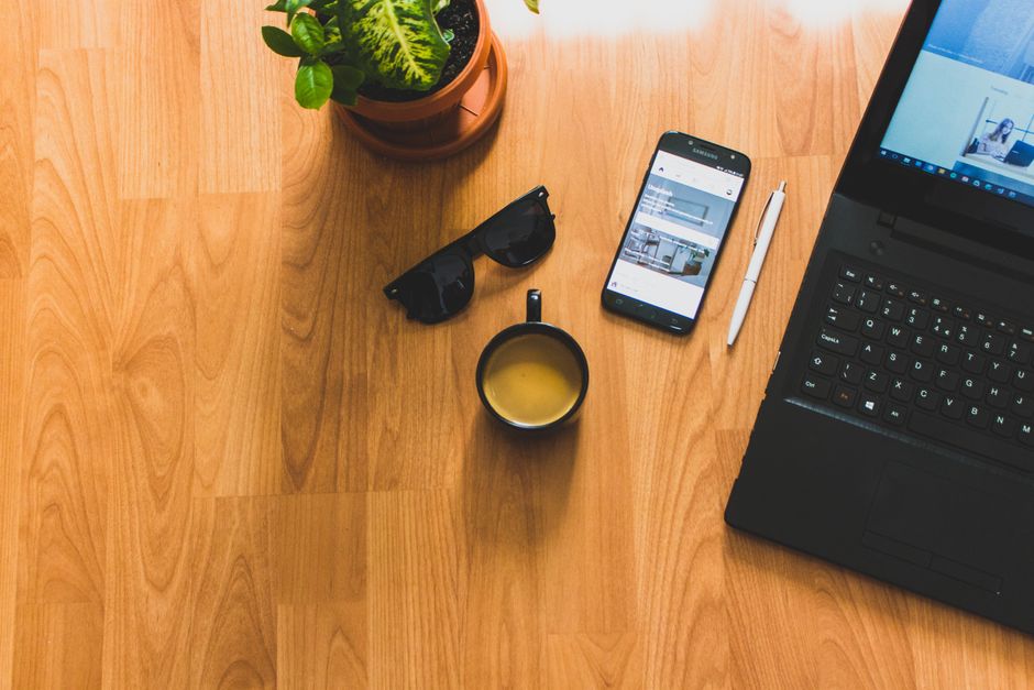 A cozy home office setup featuring a laptop, coffee mug, smartphone, and potted plant, perfect for productivity.