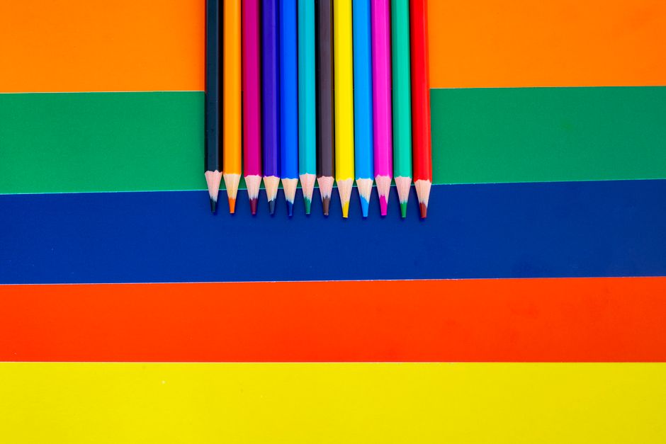 A collection of colored pencils arranged on a bright striped background, showcasing vivid rainbow hues.