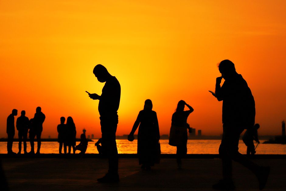 A group of silhouettes against a vibrant orange sunset by the sea, depicting serene evening moments.