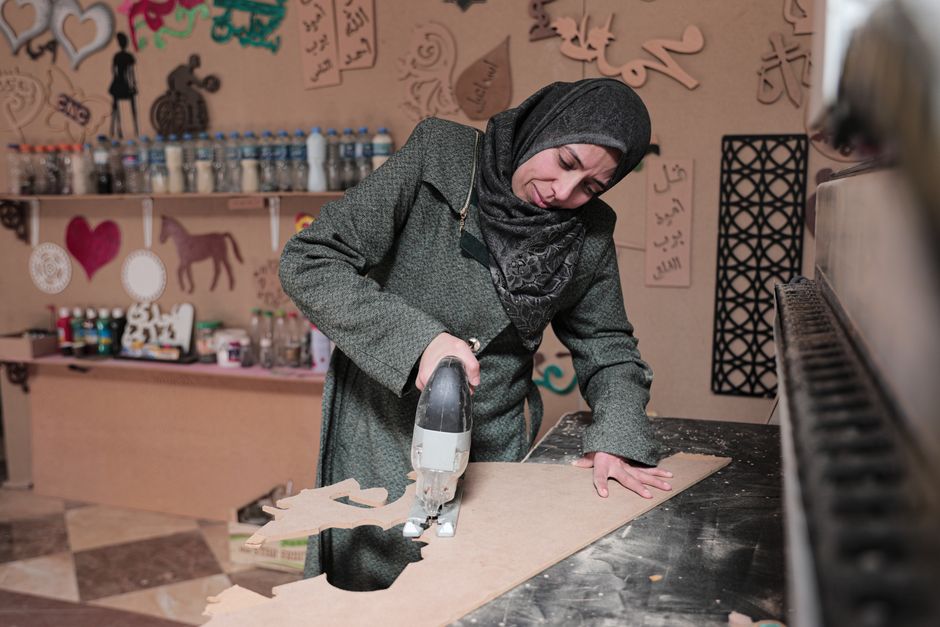 A Middle Eastern woman wearing a hijab skillfully works with wood in a creative Gaza workshop.