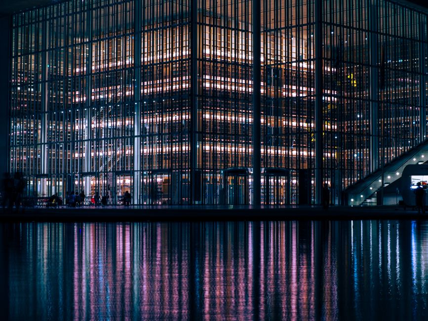 Illuminated modern glass building with stunning night reflections in water.