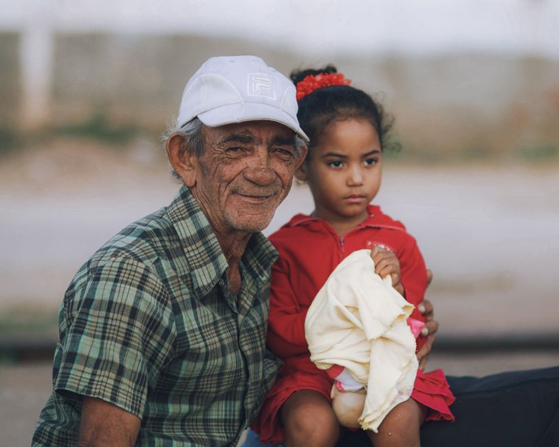 A touching portrait of a grandfather smiling while holding his thoughtful granddaughter outdoors.