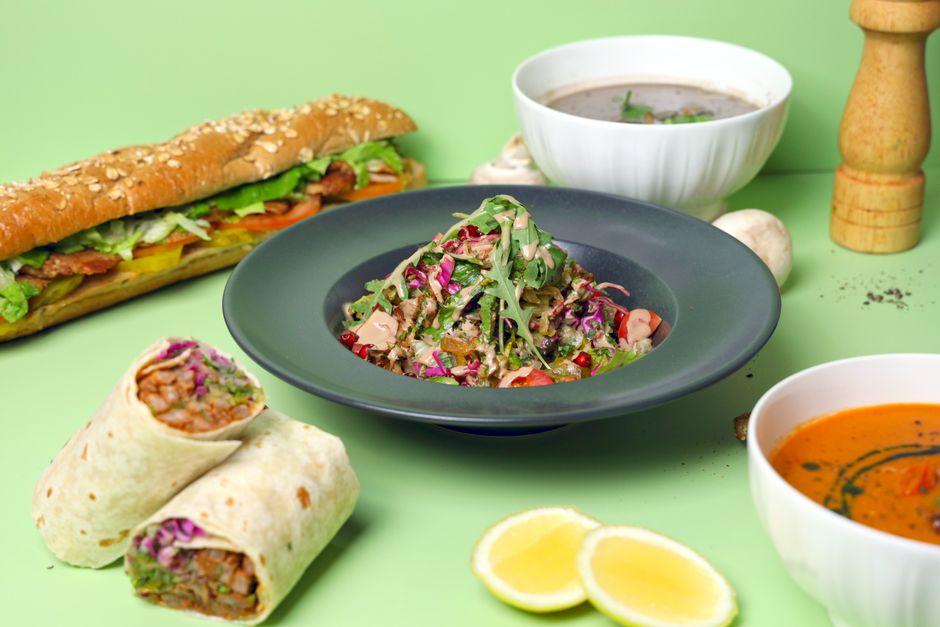 A vibrant display of healthy salad, wraps, soup, and sandwich on a green background.