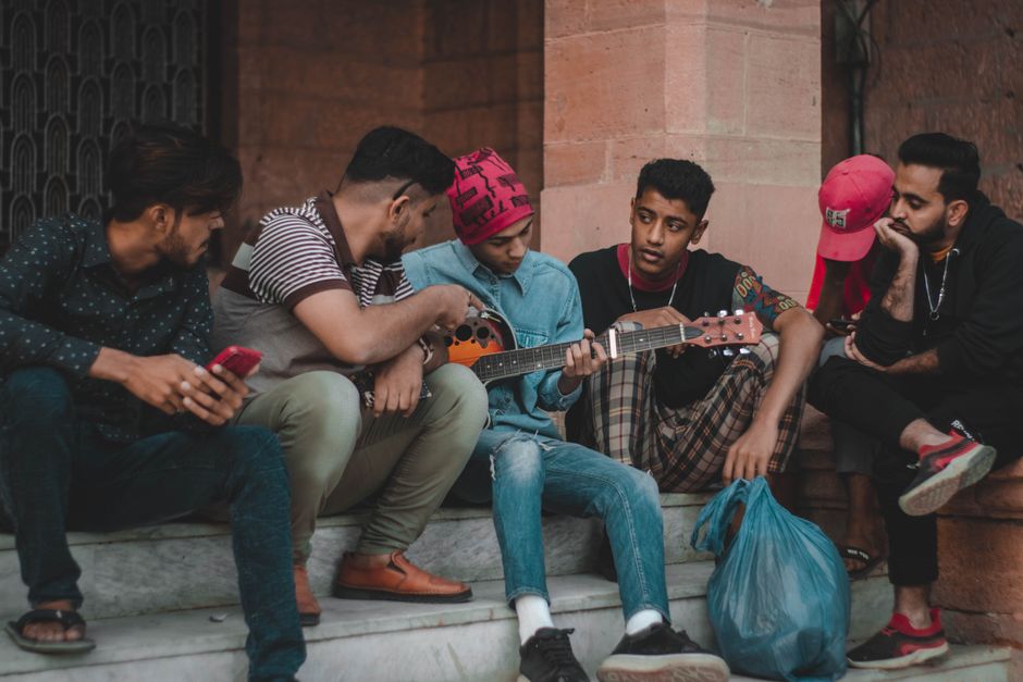 Group of young men bonding and playing guitar on city steps.