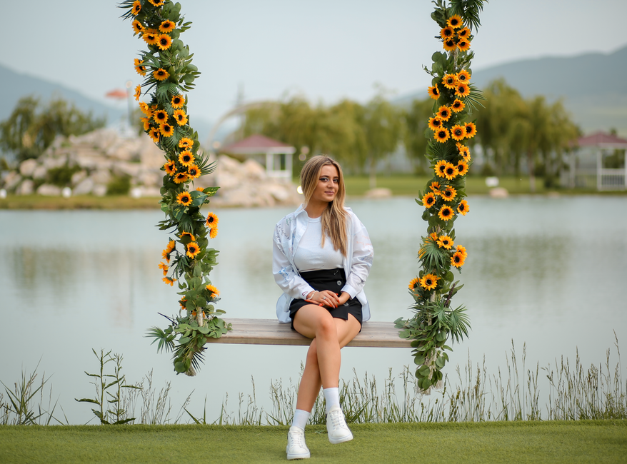 A woman enjoys a relaxing moment on a sunflower-decorated swing by a serene lakeside.