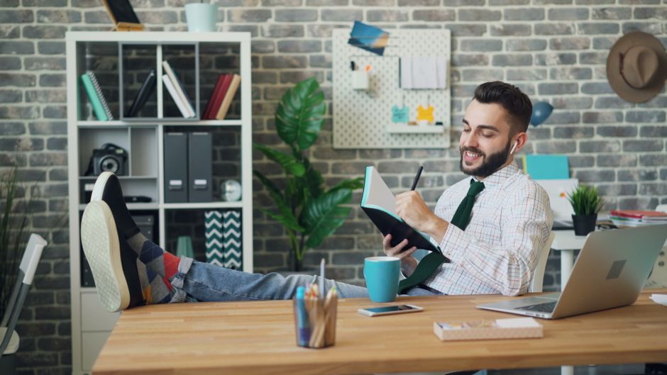 Relaxed young man in office with notebook and laptop, embodying modern work culture.