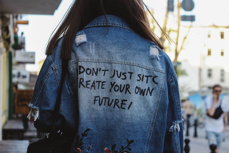 Back view of a woman in a denim jacket with an inspiring message on an urban street.