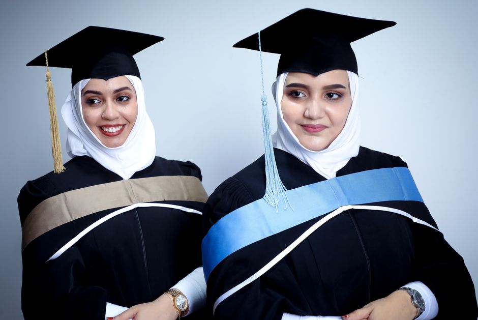 Two women in graduation attire, smiling and celebrating their academic achievements.