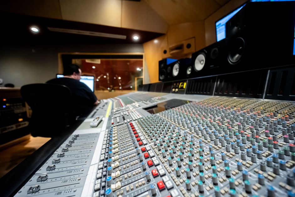 Close-up of a modern mixing console in a music recording studio with a sound engineer in the background.