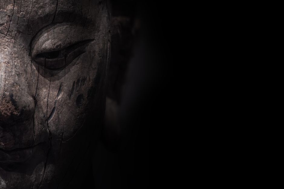 Detailed close-up of a textured wooden Buddha statue with dark, moody lighting.
