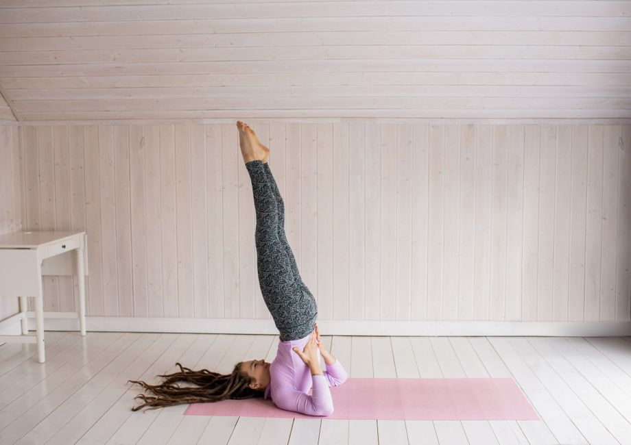 Woman in a yoga pose on a pink mat indoors, demonstrating flexibility and balance.