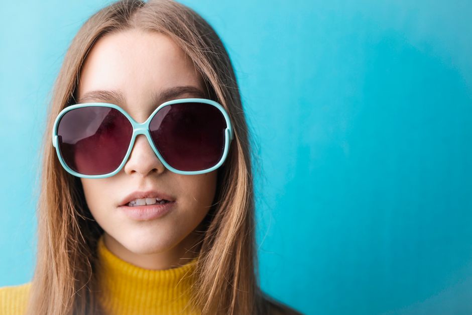 Fashion portrait of a woman in sunglasses and yellow sweater against a vibrant blue background.