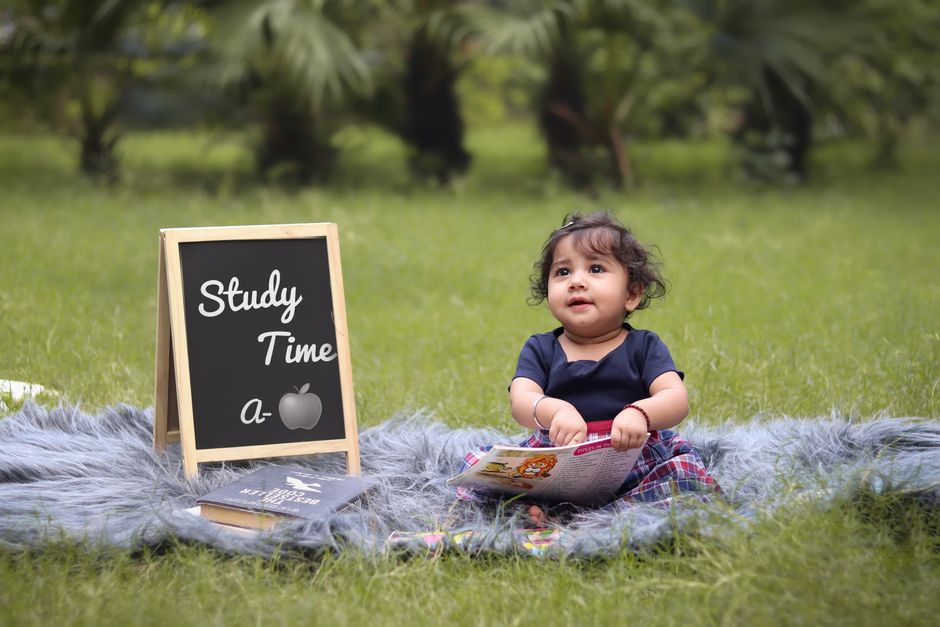 Cute baby sitting outdoors on a blanket with books and a chalkboard labeled 'Study Time a-apple'.