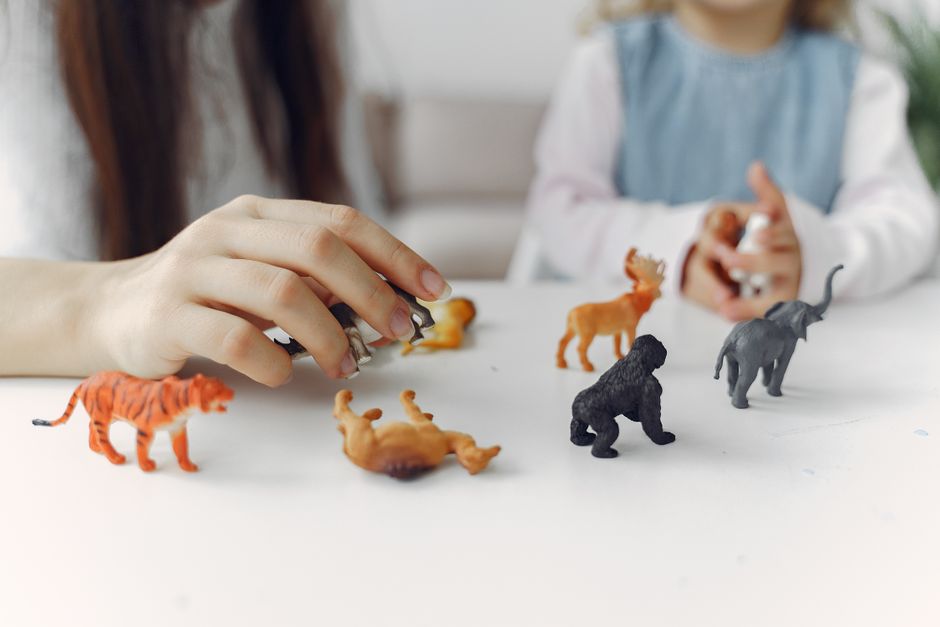 Crop mother and daughter playing with small toy wild animals for early education and development during spending time together at home