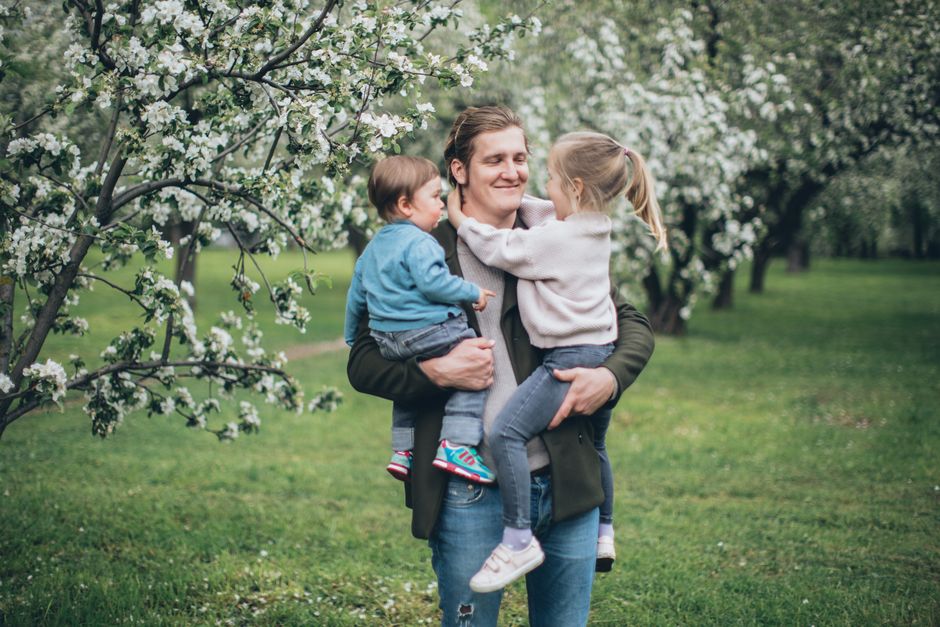 A loving father holds his children among blooming spring trees.