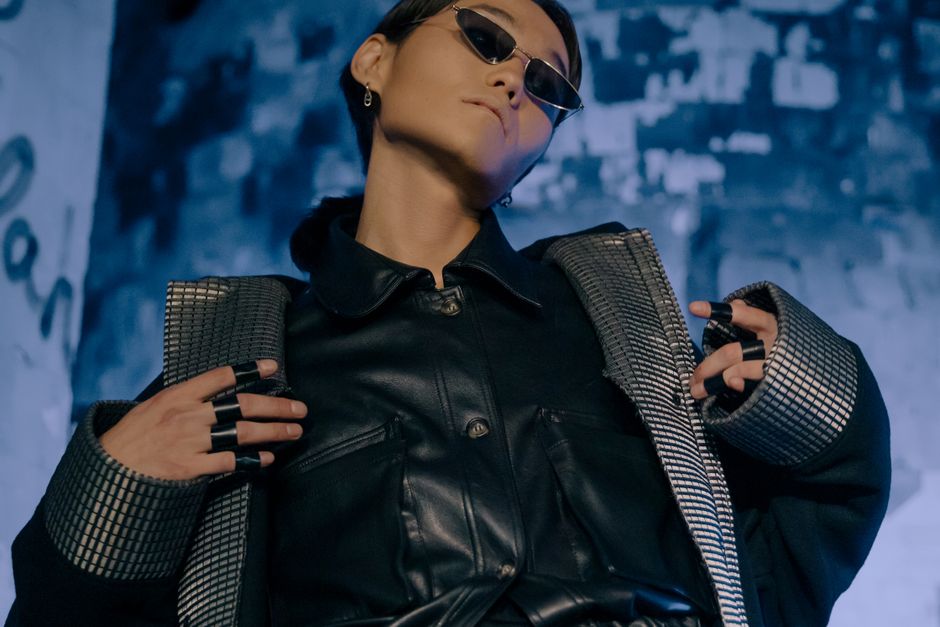 A stylish model poses in leather attire and sunglasses, embodying a modern, futuristic fashion concept.