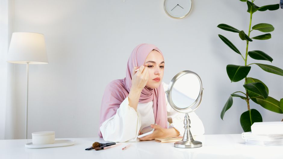 A woman in a hijab applying makeup in a modern, well-lit room.