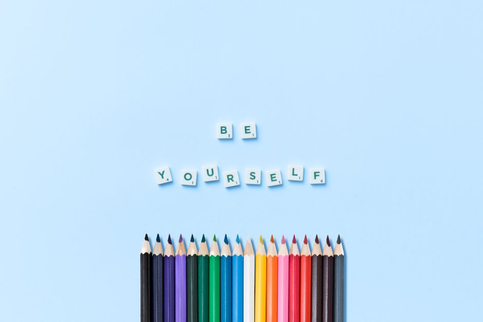 Top view of colorful pencils and 'Be Yourself' message on a blue background.