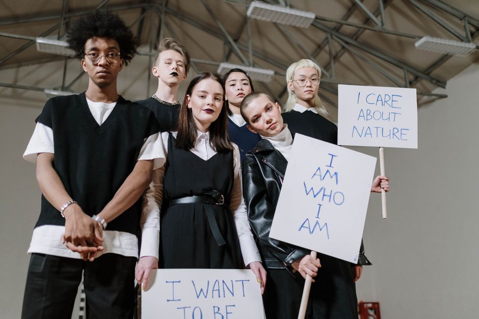 A diverse group of teenagers holding protest signs indoors, advocating individuality and environmental care.