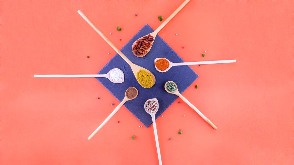 A vibrant flat lay of assorted spices in wooden spoons on a colorful background.