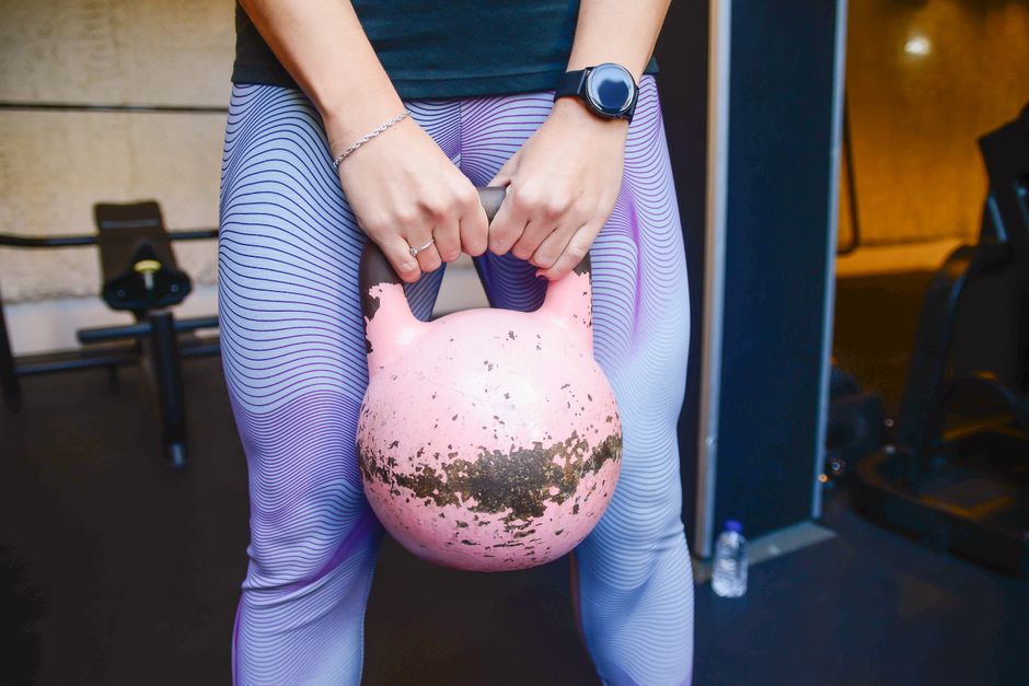 Fit woman holding a pink kettlebell during a workout session indoors.