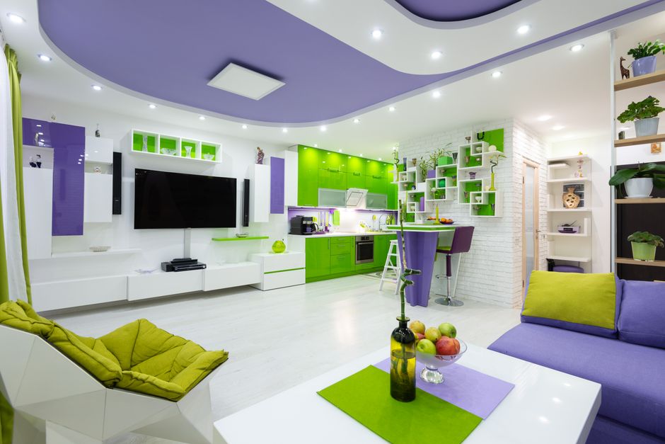Comfy sofa with armchair and coffee table placed in front of modern TV set in spacious studio apartment near kitchen with bright green cabinets and counter