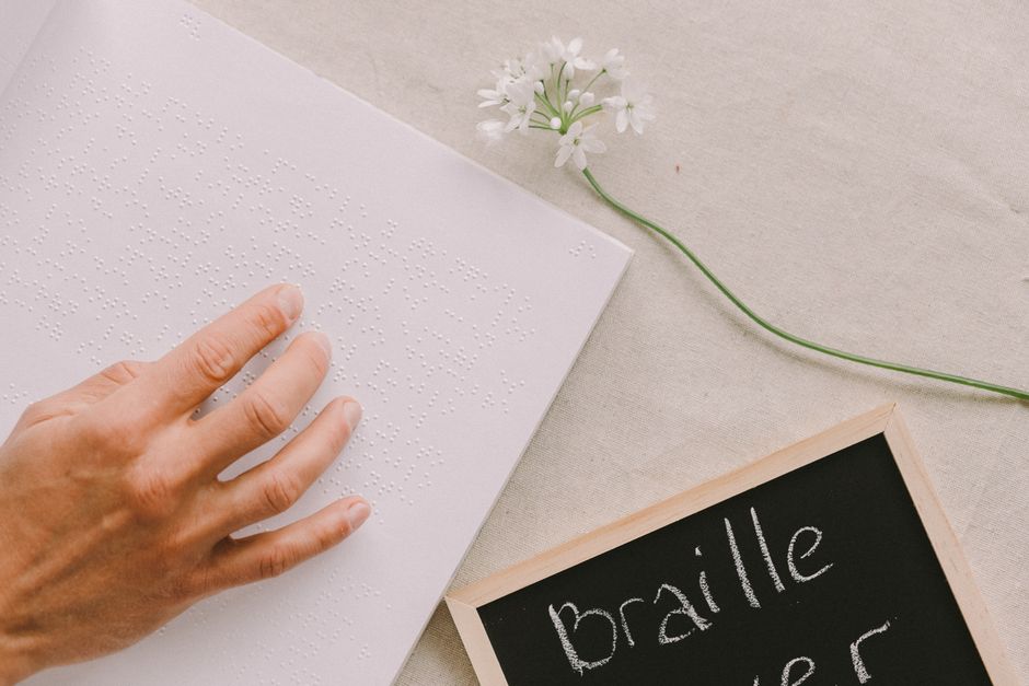 A person gently reads a Braille book, symbolizing sensory perception and independence.