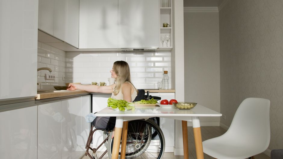 Woman in wheelchair preparing food in a modern kitchen with fresh vegetables.