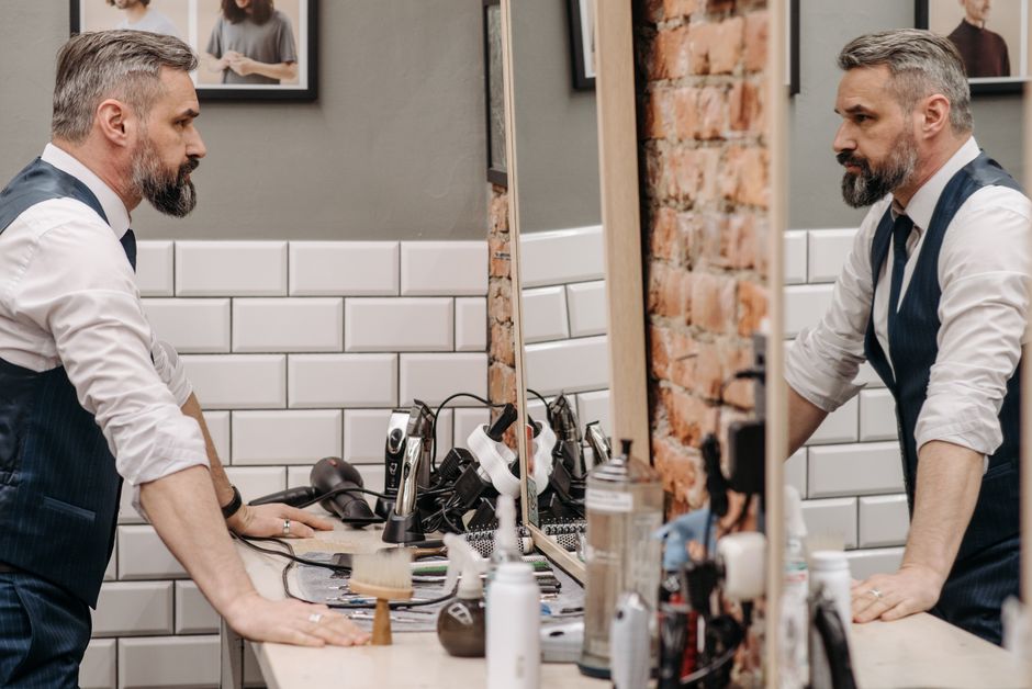 A bearded gentleman examines his reflection in a stylish barbershop setting.