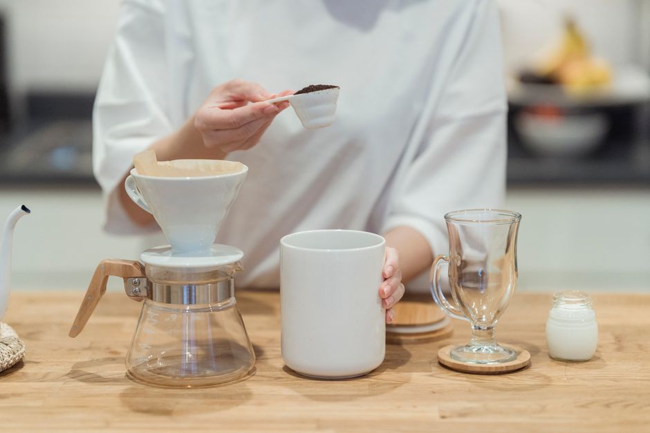 A person prepares a pour-over coffee using a manual drip coffee maker in a bright kitchen.