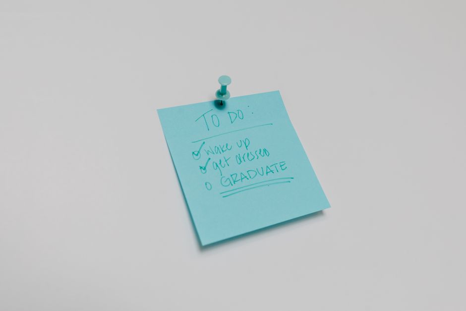 A blue sticky note with a graduation to-do list pinned to a white surface.