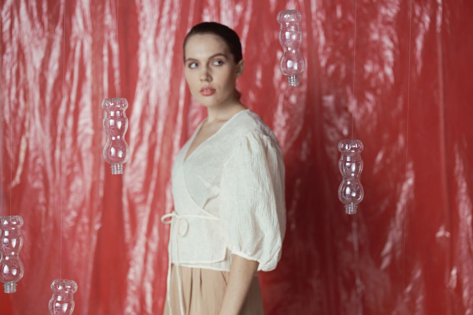 Elegant woman in studio with hanging recycled plastic bottles art installation.