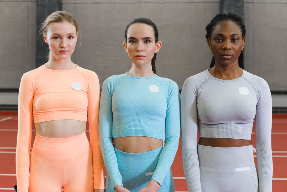 Three women posing confidently in vibrant activewear indoors on a track.