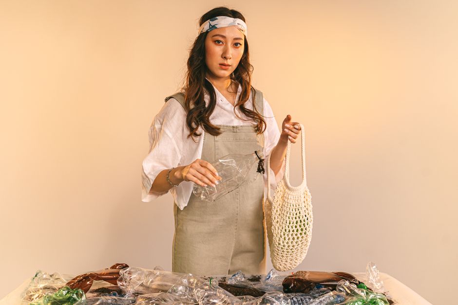 Young woman in studio with mesh bag holding plastic for recycling, promoting zero waste.