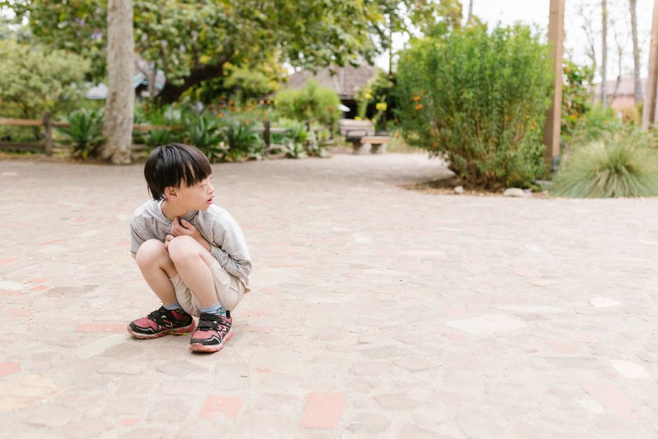Young Asian boy sitting outdoors looking thoughtful, surrounded by nature.