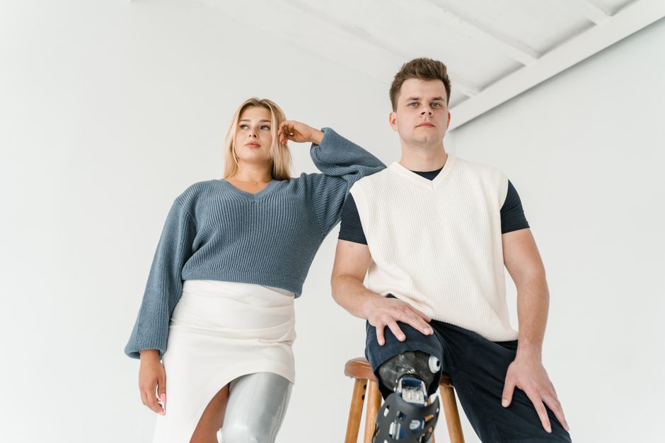 A fashionable studio portrait featuring two models with prosthetic legs posing confidently.