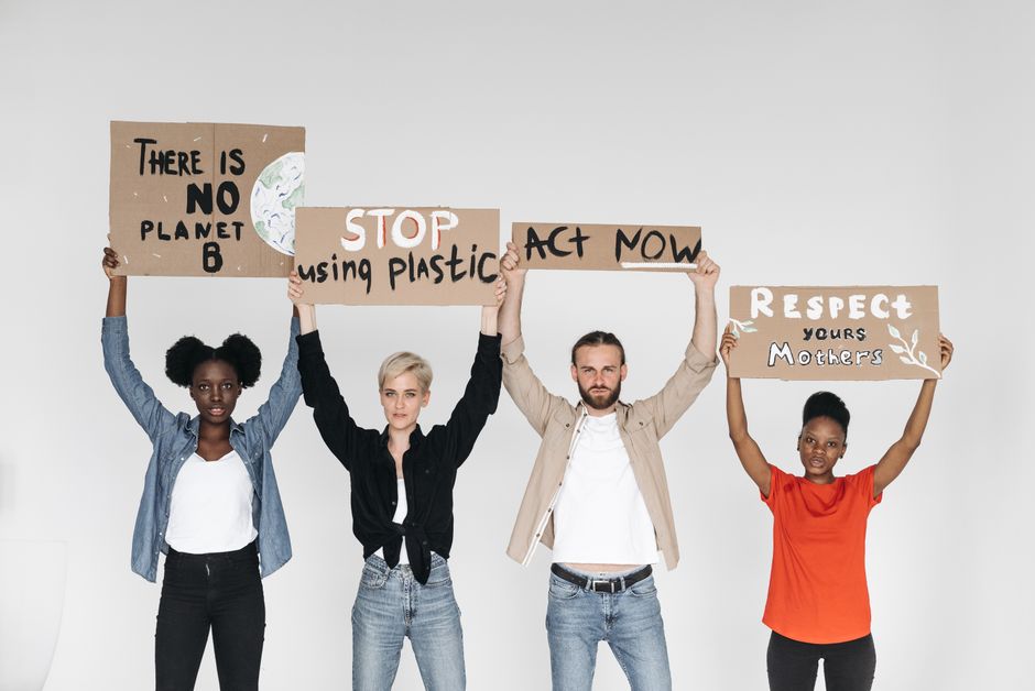 Four diverse individuals hold protest signs advocating for environmental change in a studio setting.