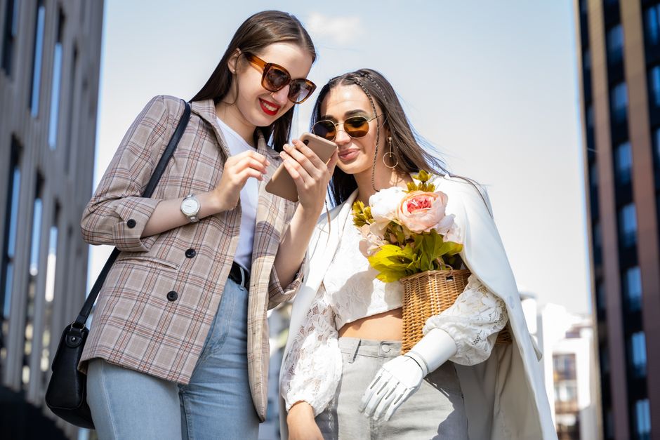 Two stylish women enjoy moments in the city with flowers and phones on a sunny day.
